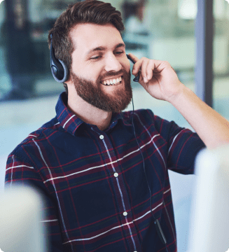 A smiling man in a plaid shirt enjoying a call to action or a conversation through his over-ear headphones.